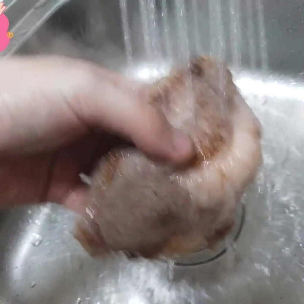 Una pieza de costilla de res blanqueada siendo enjuagada bajo agua corriente en un fregadero.