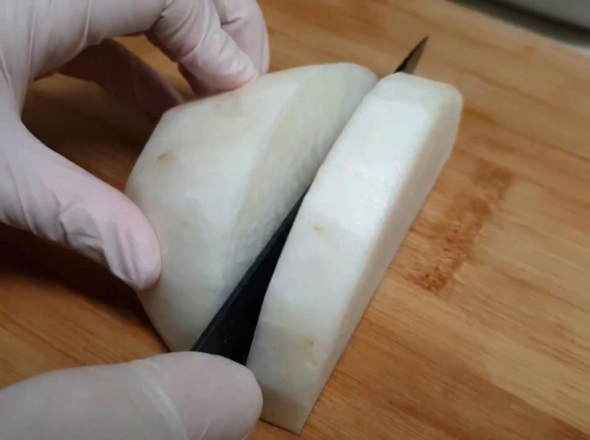 Rábano blanco siendo cortado en una tabla de madera con un cuchillo de cocina, manos usando guantes de seguridad alimentaria.