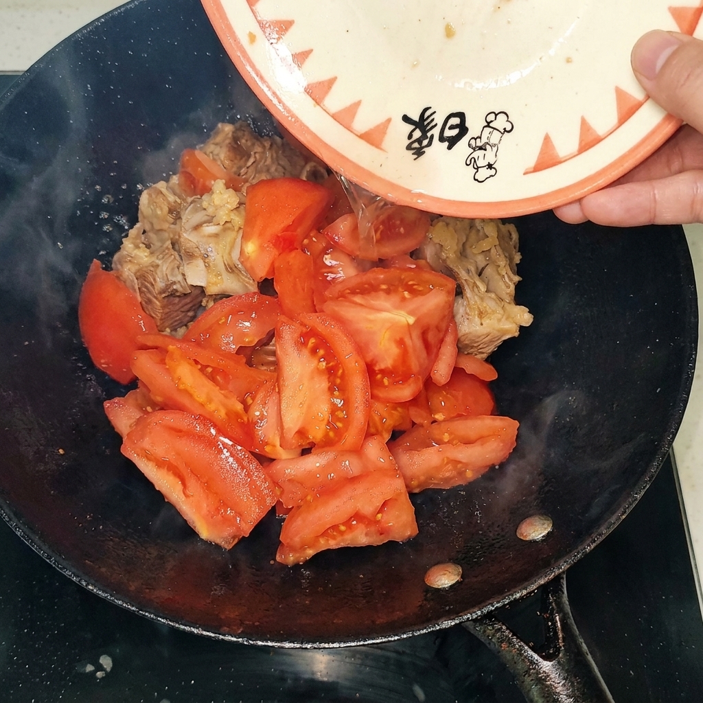 Trozos de tomate pelado siendo añadidos al wok con las costillas de res selladas.