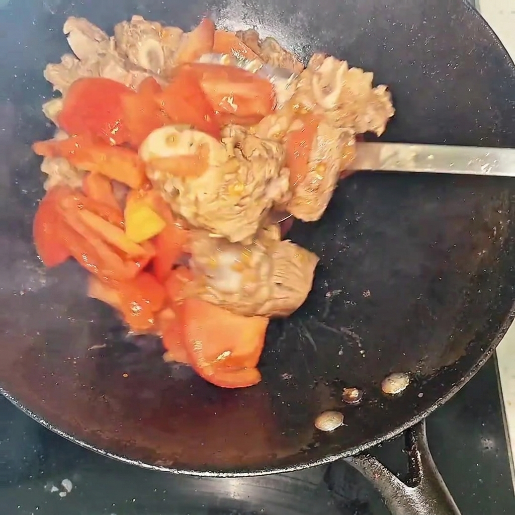 Un primer plano de las costillas de res y los tomates salteándose en el wok, mostrando el líquido que comienza a formarse.