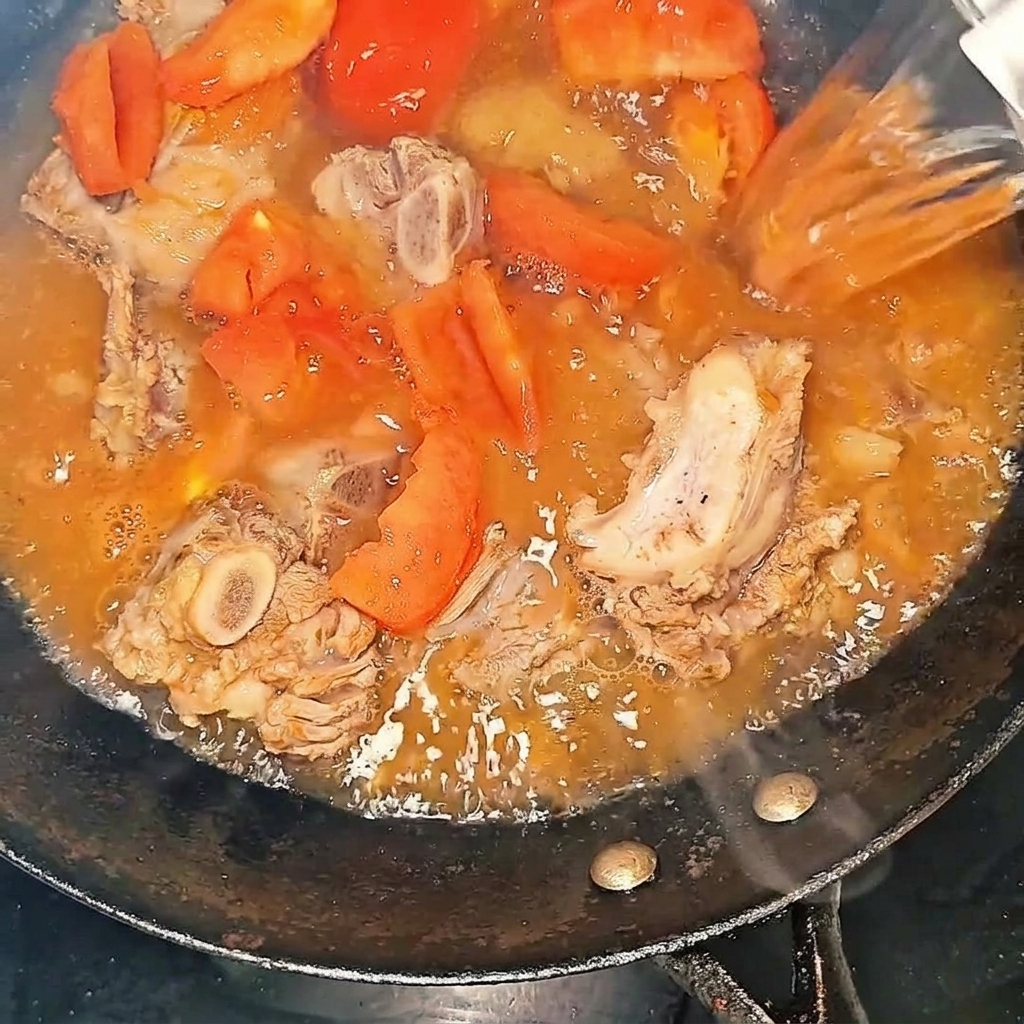 Agua caliente siendo vertida en el wok con las costillas de res y los tomates.