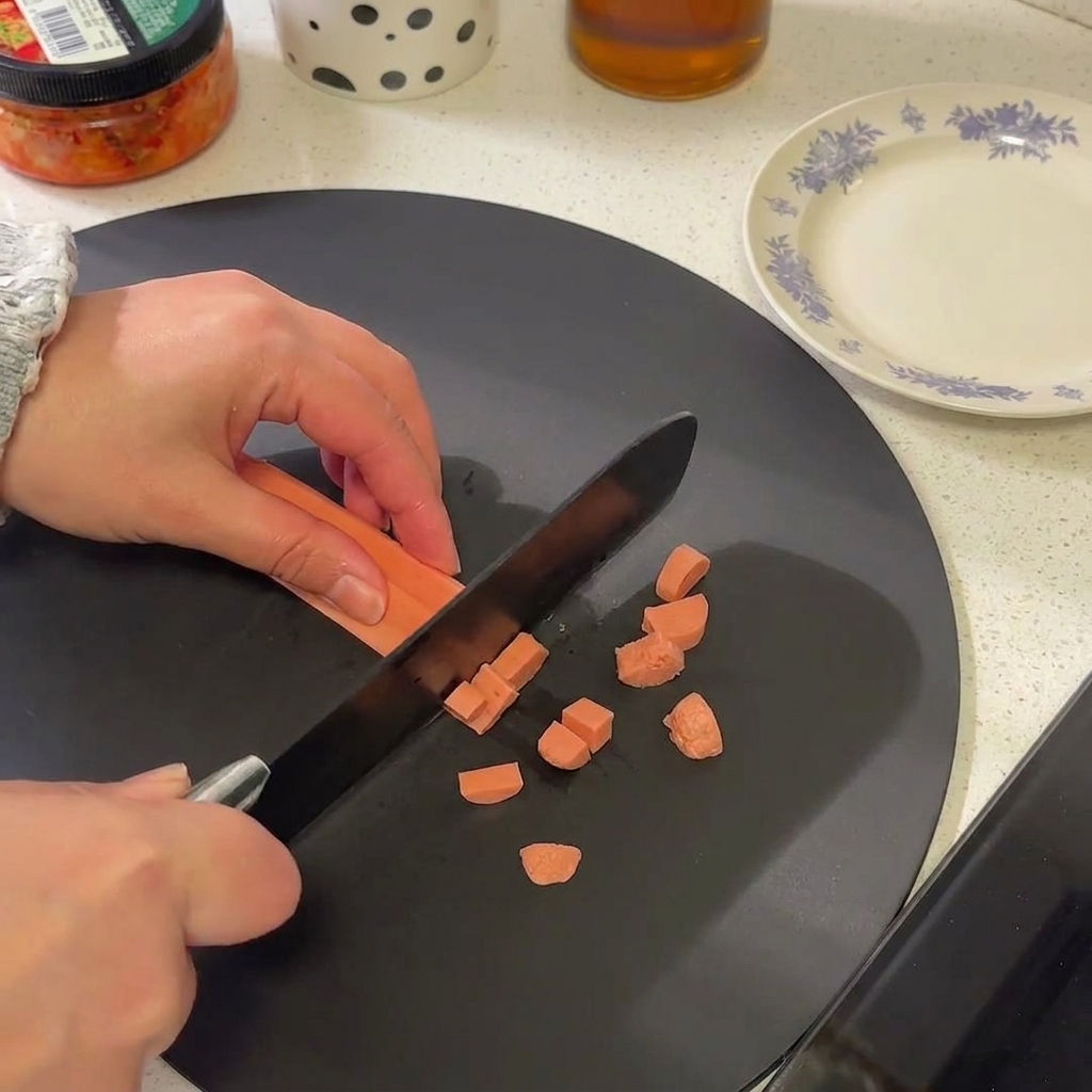 Primer plano de una salchicha siendo cortada en pequeñas rodajas circulares sobre una tabla de cortar negra.