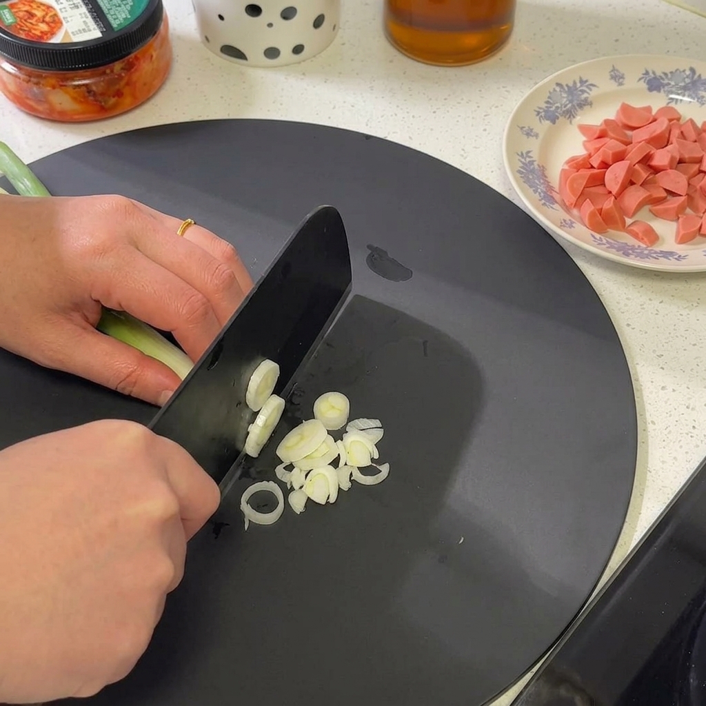 Un manojo de cebolletas siendo picadas finamente en una tabla de cortar, enfocándose en las secciones blancas y verde claro.