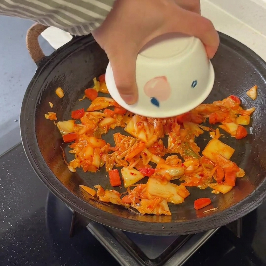 Arroz cocido sobrante siendo mezclado completamente en la base de kimchi y salchicha en una sartén caliente.