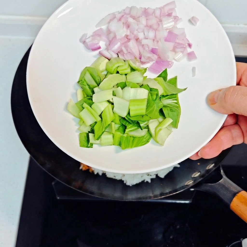 Vertiendo cebollas moradas en dados y bok choy picado desde un plato blanco hacia el wok con el arroz frito.
