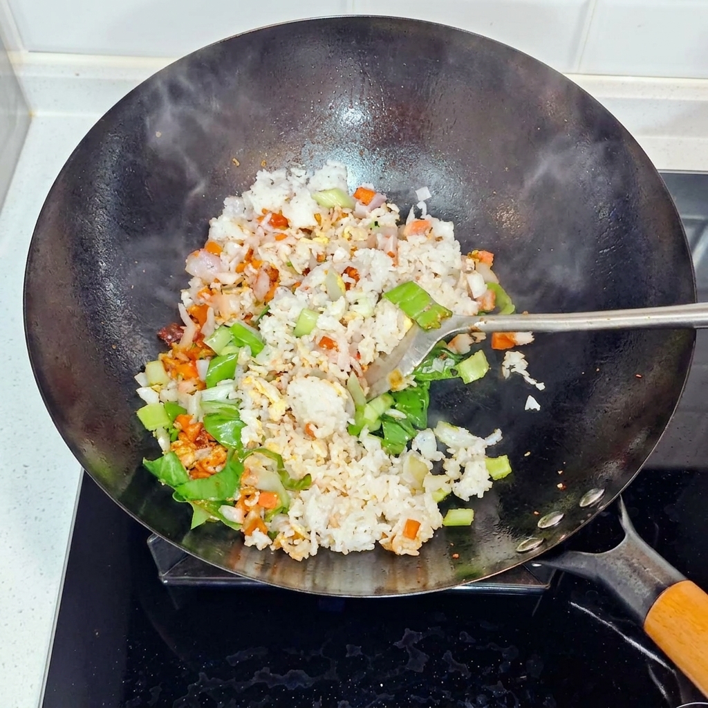 Arroz, cebollas y bok choy siendo revueltos y salteados en un wok.