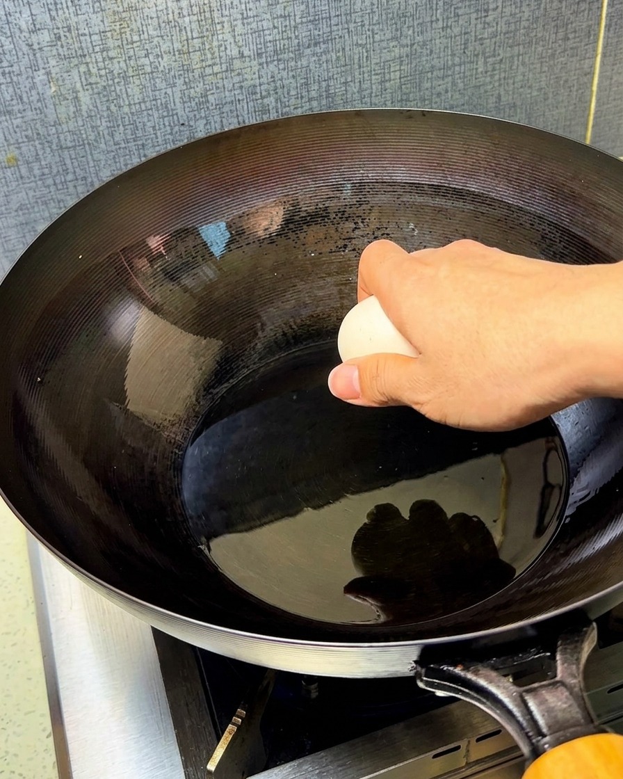 Dos huevos crudos cayendo sobre un wok caliente con aceite brillante.