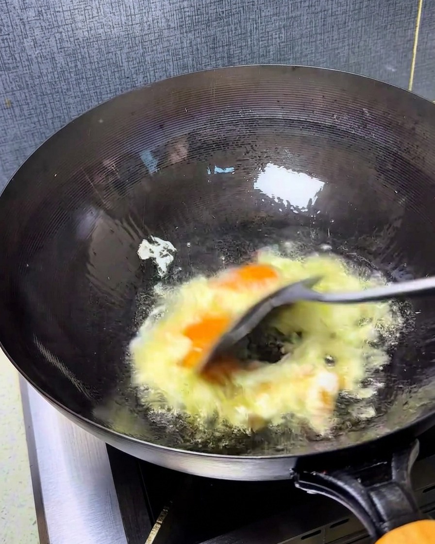Huevos siendo revueltos rápidamente en un wok caliente con una espátula.