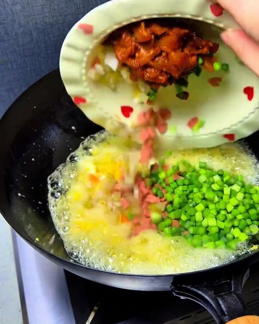 Kimchi, jamón, pollo y brotes de ajo vertidos en el wok con los huevos.