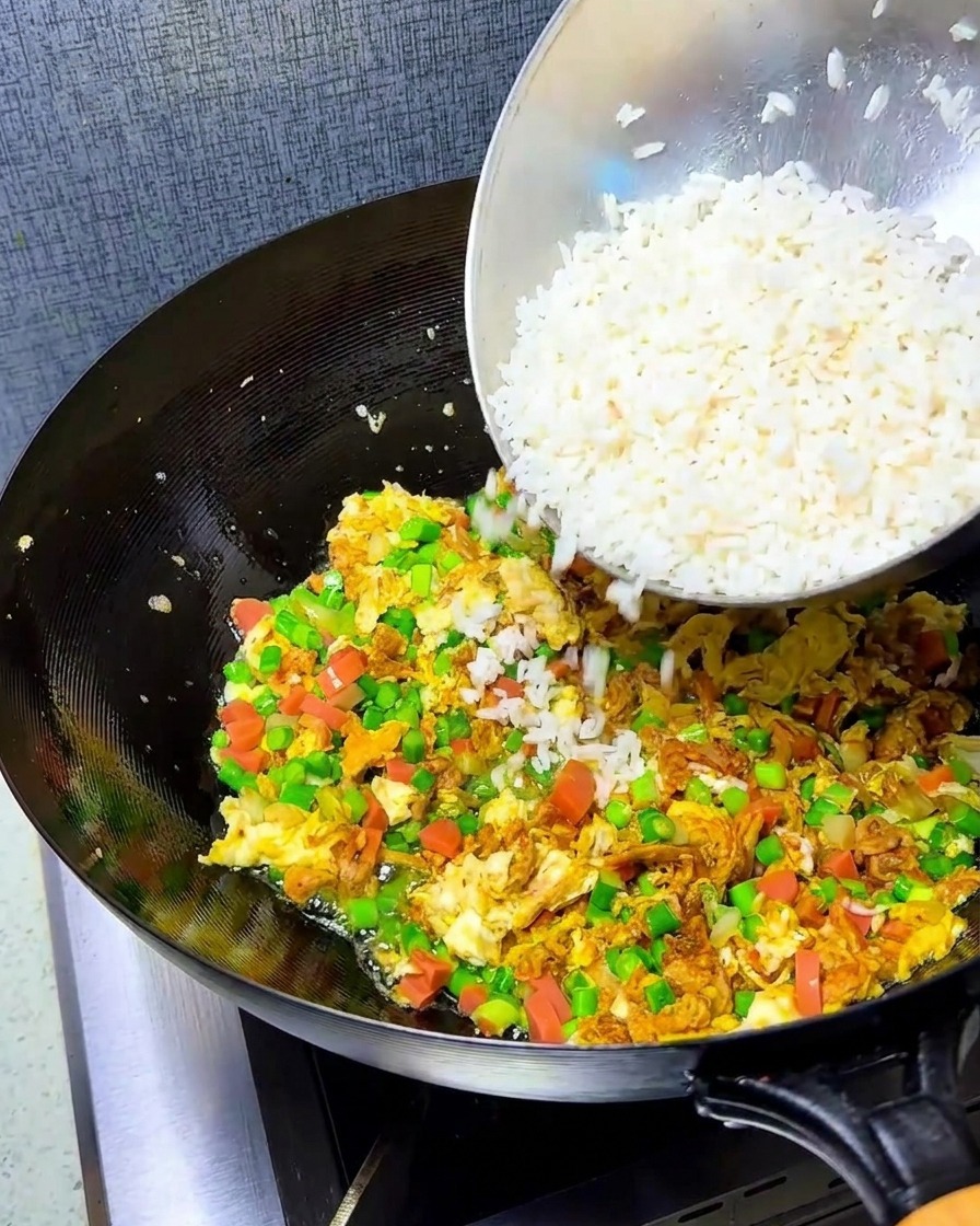 Arroz desmenuzado siendo añadido al wok con los ingredientes ya salteados.