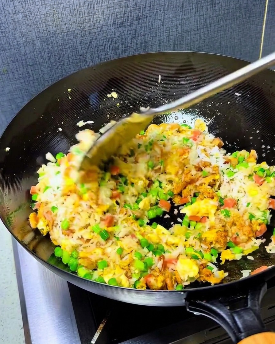 Una cucharada de aceite de chile rojo siendo añadida al arroz en el wok.
