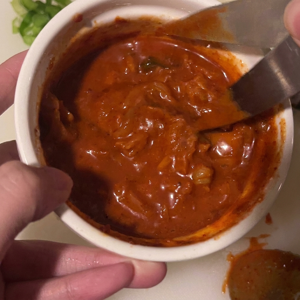 Unas tijeras cortando trozos de kimchi directamente dentro de un tazón con salsa.