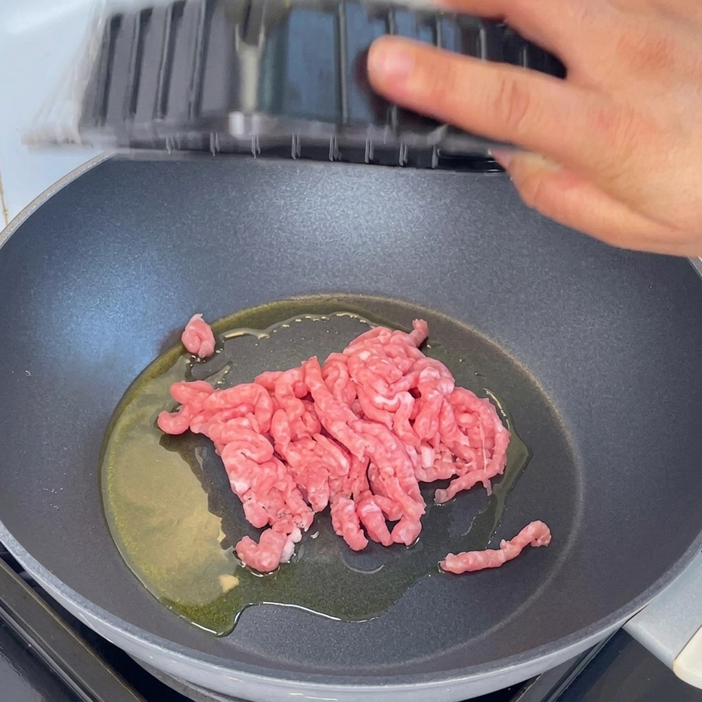 Cerdo picado siendo añadido a una sartén con aceite caliente y salteado con una espátula de madera.