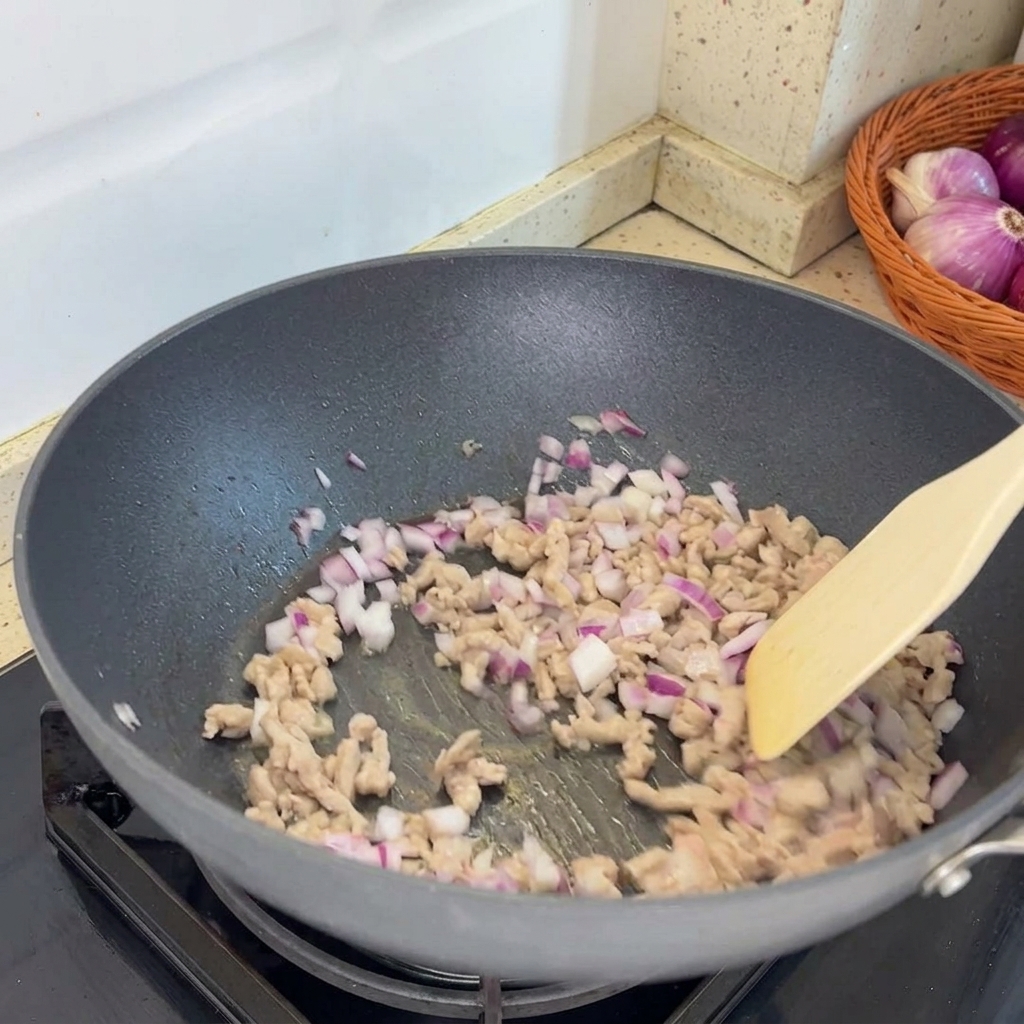 Chalotas picadas siendo añadidas a la sartén y combinadas con el cerdo picado ya cocinado.