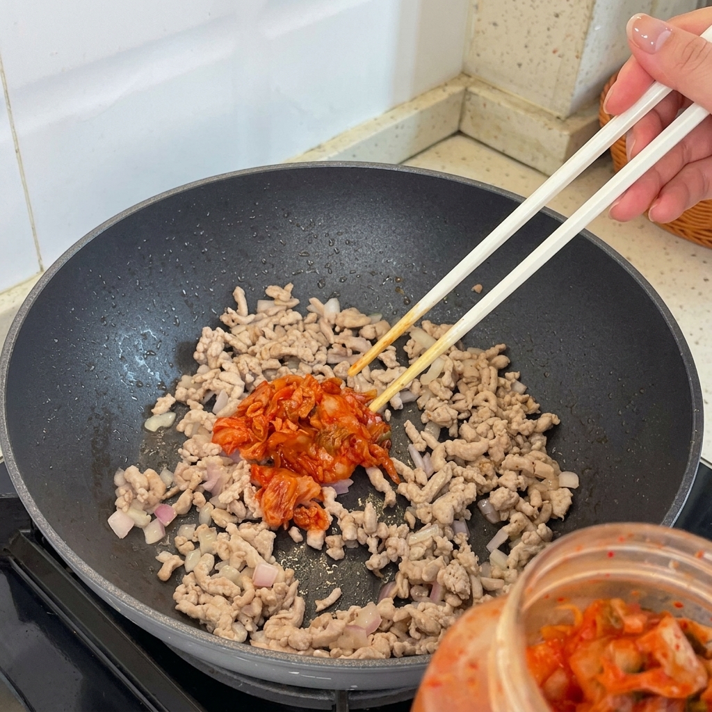 Trozos de kimchi siendo añadidos a la mezcla de carne y chalotas en la sartén.