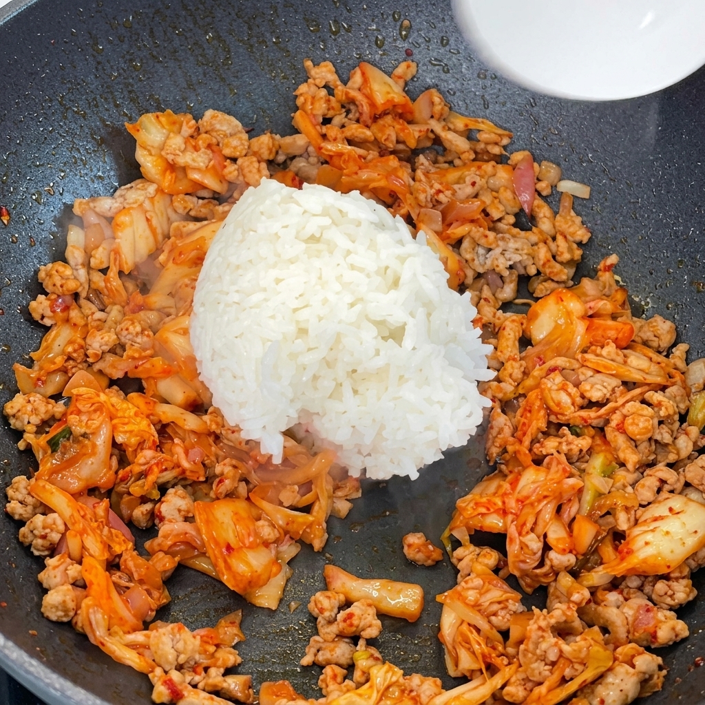 Arroz blanco cocido siendo añadido a una sartén llena con la mezcla de cerdo y kimchi.