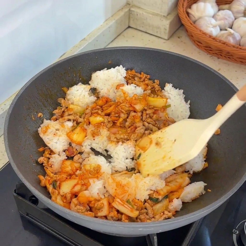 Una espátula mezclando vigorosamente el arroz con la carne y el kimchi en un wok caliente.