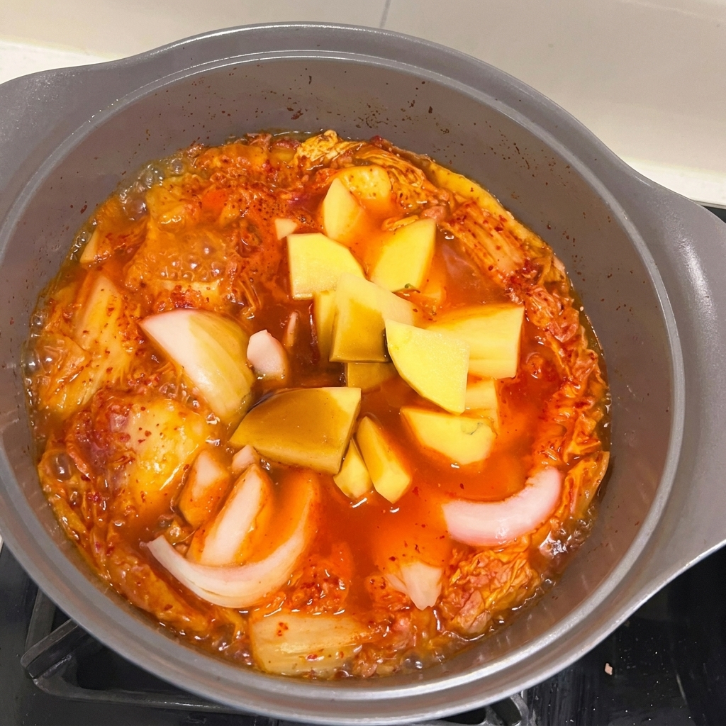 Trozos de cebolla y patata añadidos al guiso de Spam y kimchi.