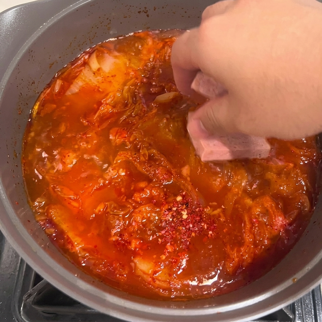 Rodajas de tofu colocadas cuidadosamente en el guiso de kimchi rojo hirviendo.