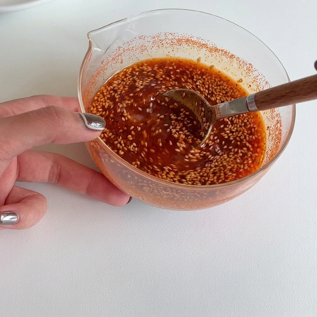 Mano revolviendo una salsa roja suave y vibrante en un tazón de vidrio con una cuchara de madera hasta que esté perfectamente combinada.