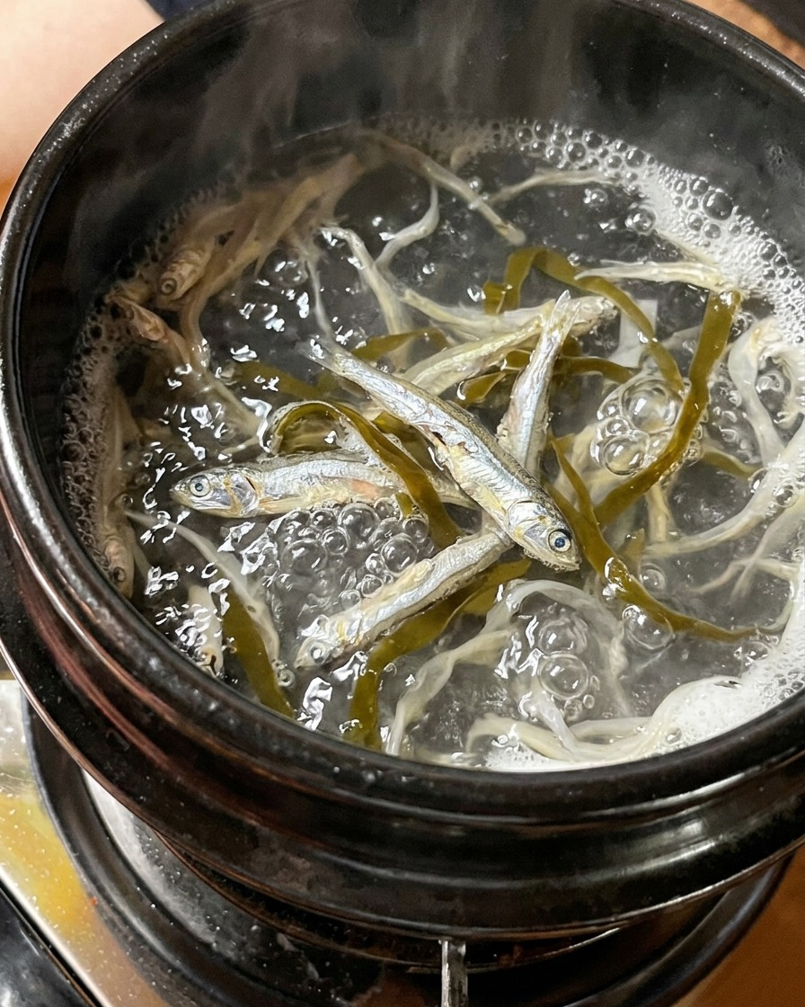 Anchoas secas y trozos de alga hirviendo en una olla de agua.