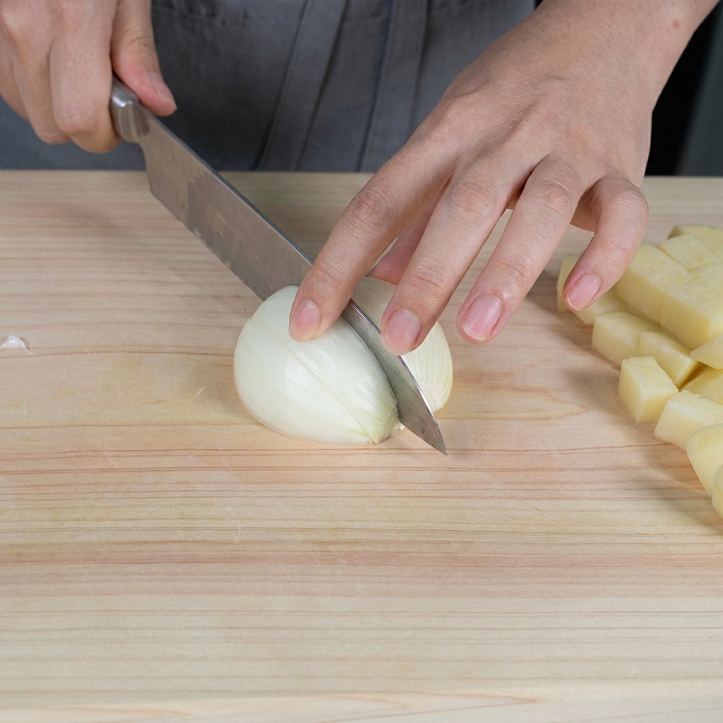 Manos picando una cebolla blanca cruda en trozos pequeños sobre una tabla de madera clara.