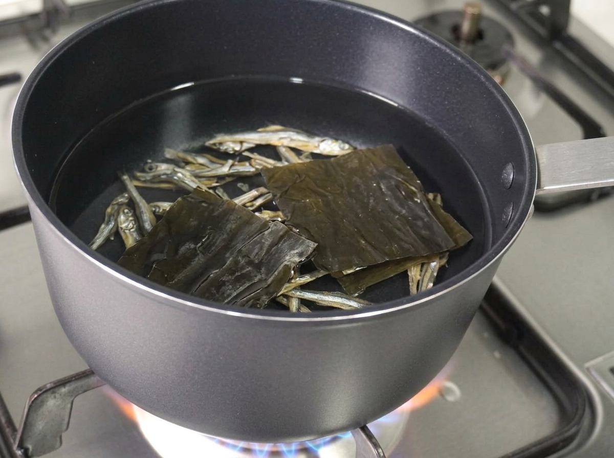 Anchoas secas y un trozo cuadrado de alga seca flotando en la olla de agua.