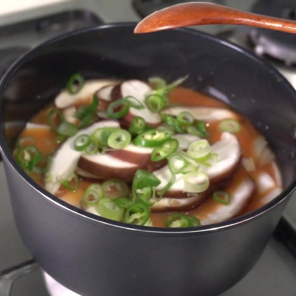 Chiles verdes rebanados y cebolletas siendo espolvoreados en un guiso burbujeante.