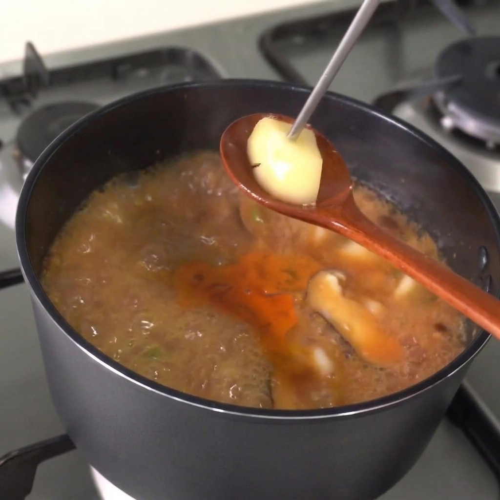 Una cuchara de madera levantando un trozo de patata cocida del guiso hirviendo para comprobar su cocción.