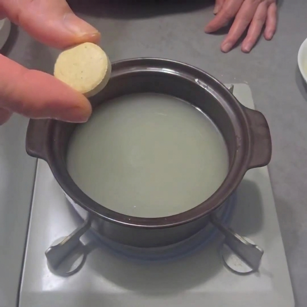 Un cubito de caldo de marisco siendo añadido a una olla con agua en la estufa.