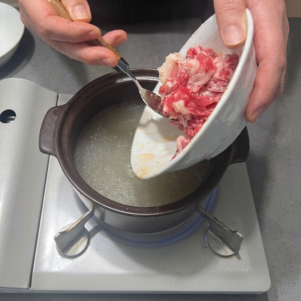 Lonchas de falda de ternera siendo añadidas a la olla con el caldo sazonado.