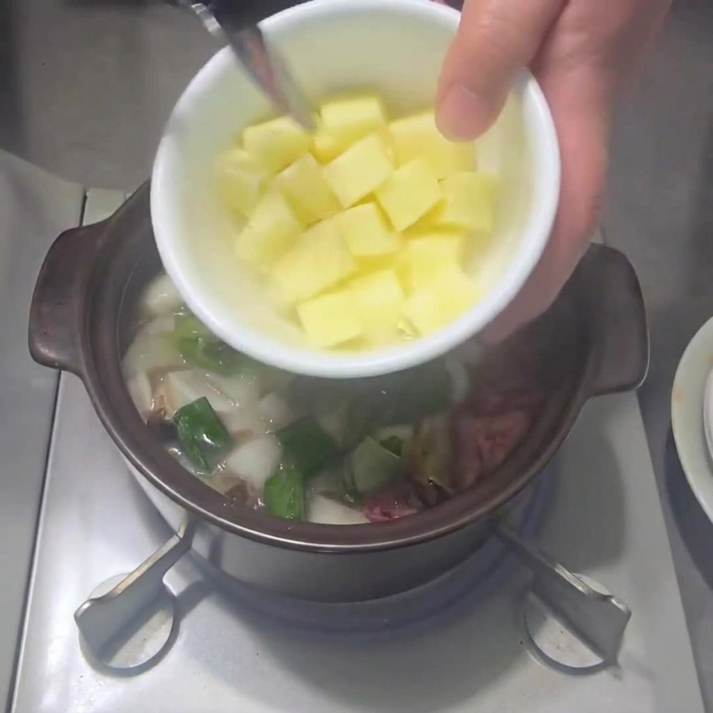 Patatas cortadas en cubos siendo añadidas a la olla con las verduras.