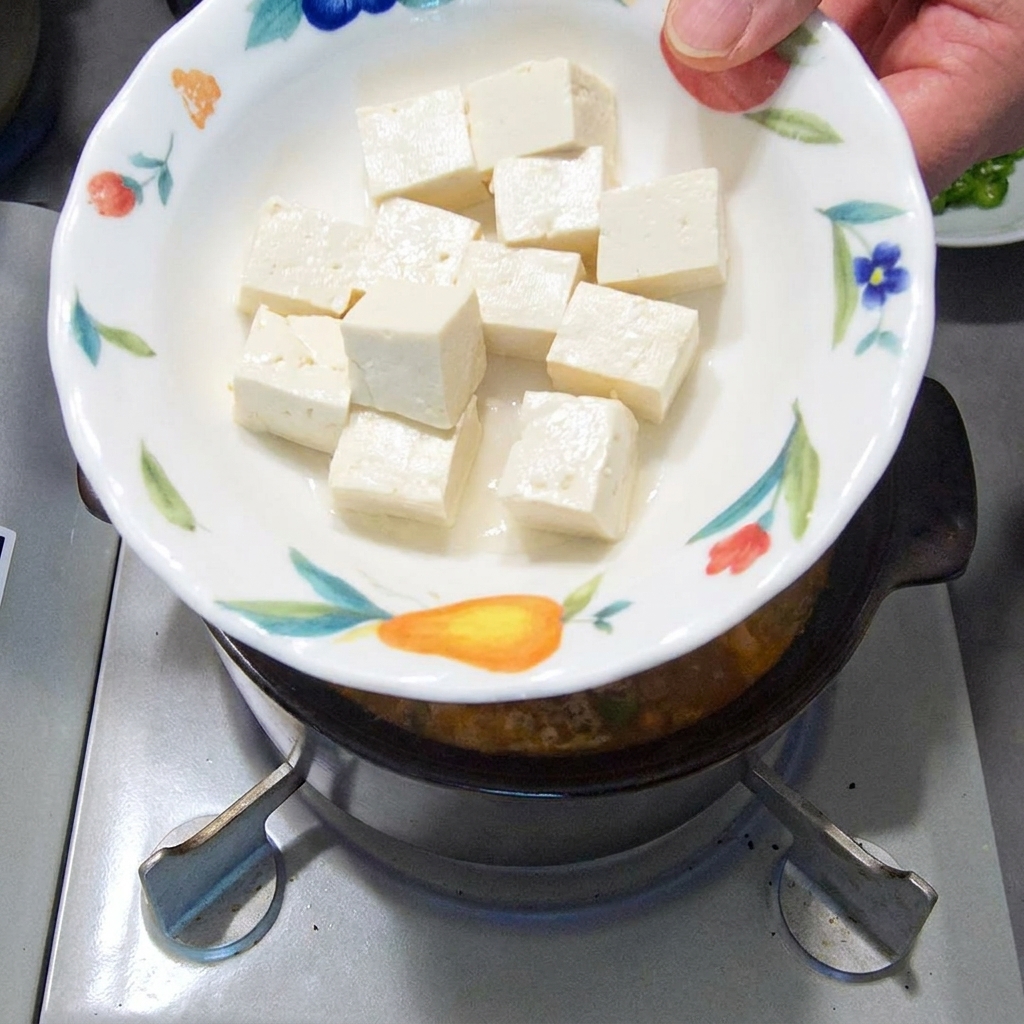 Cubos de tofu suave siendo añadidos al estofado a fuego lento.