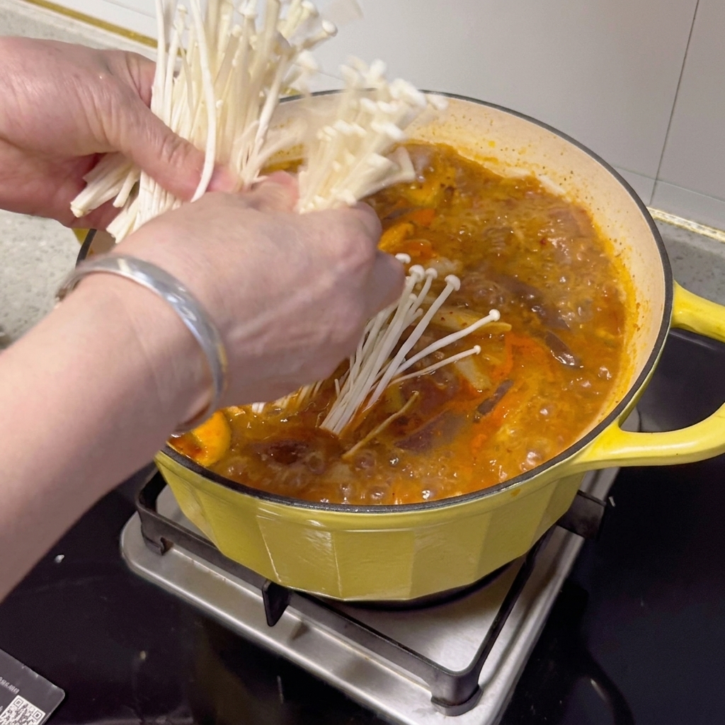 Setas enoki frescas, cebolletas y rodajas de chile dispuestas sobre el estofado terminado.