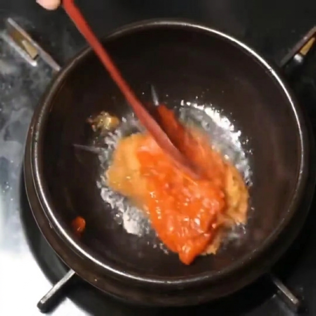 Mezcla espesa de pasta roja y marrón removida con una cuchara de madera en una olla negra a fuego lento.