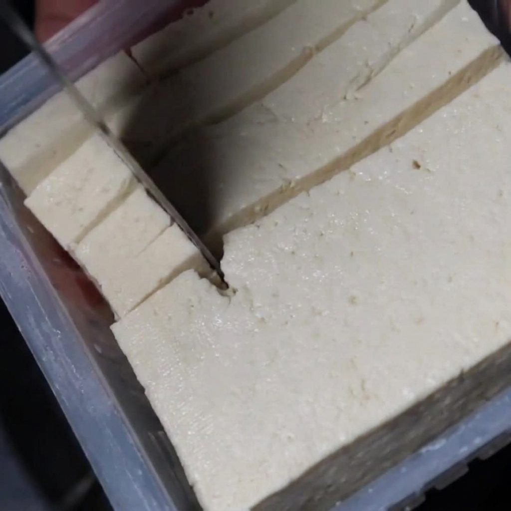 Dados de tofu blanco del tamaño de un bocado siendo añadidos al estofado hirviendo a fuego lento.