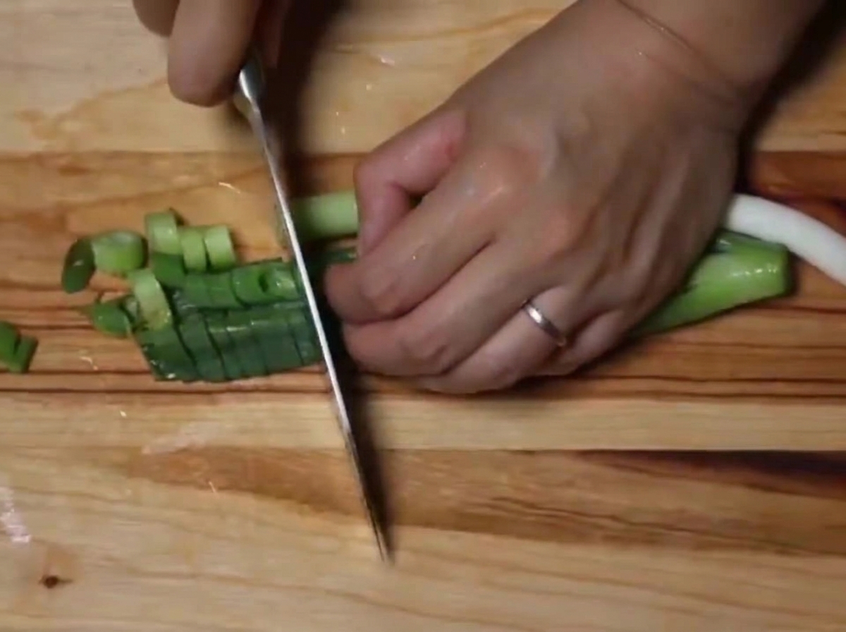 Primer plano de cebolletas frescas cortadas en pequeñas rodajas sobre una tabla de madera.
