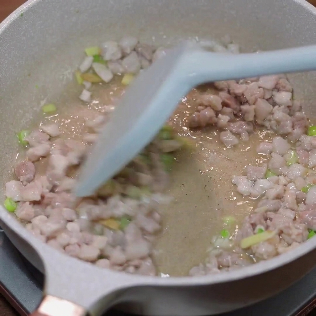 Carne de cerdo picada siendo salteada en una sartén con cebolletas y jengibre.
