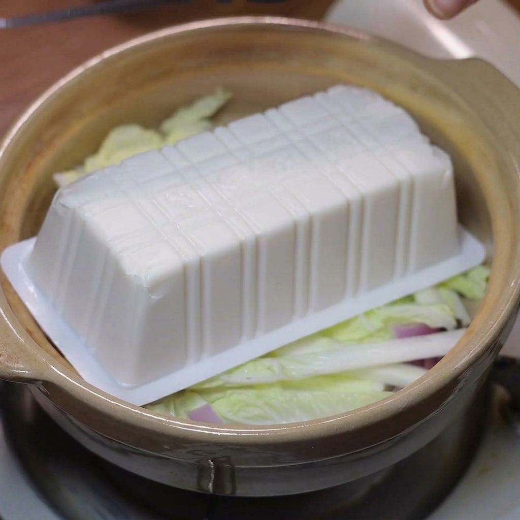 Rodajas de tofu suave colocadas sobre la col y las cebollas en la cazuela.