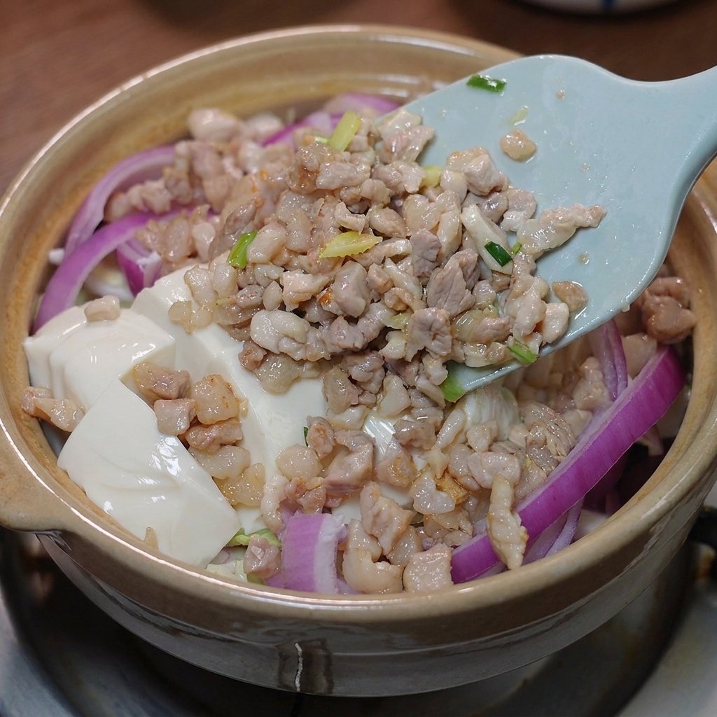 La carne salteada y la salsa preparada siendo vertidas sobre el tofu en la cazuela.