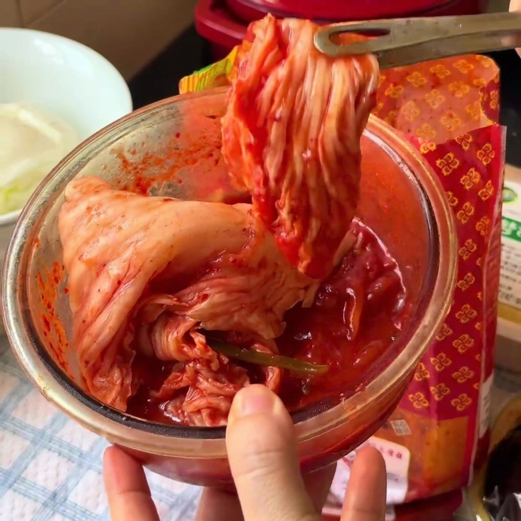Kimchi cortándose en trozos más pequeños dentro de un tazón de vidrio usando tijeras de cocina.