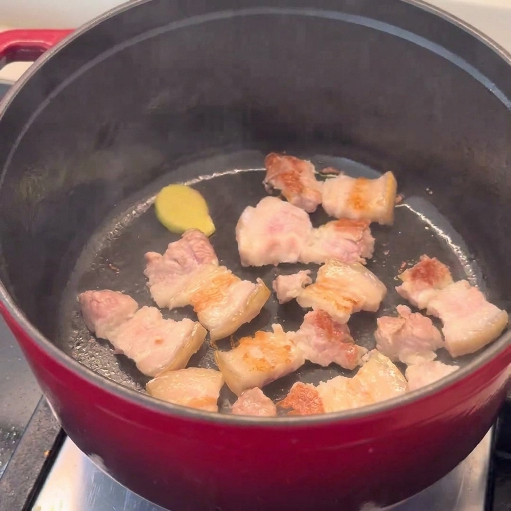 Trozos de panceta dorándose en una olla roja.