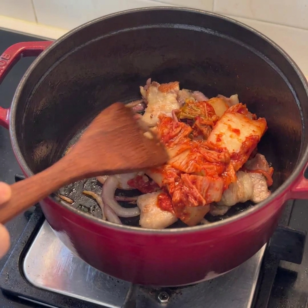 Trozos de kimchi siendo salteados junto con la panceta dorada en una olla.