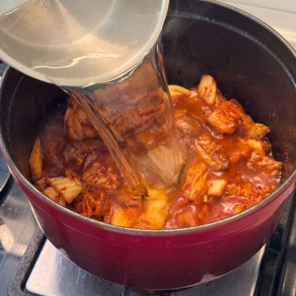 Agua vertiéndose en la olla con la carne y el kimchi, comenzando la base del estofado.