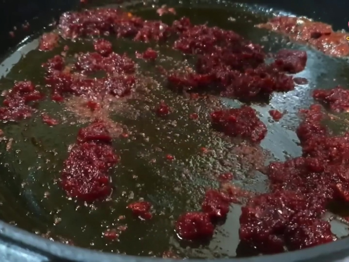 Pequeños trozos de cerdo mezclándose y sofriéndose en una sartén con una vibrante mezcla de aceite de chile.