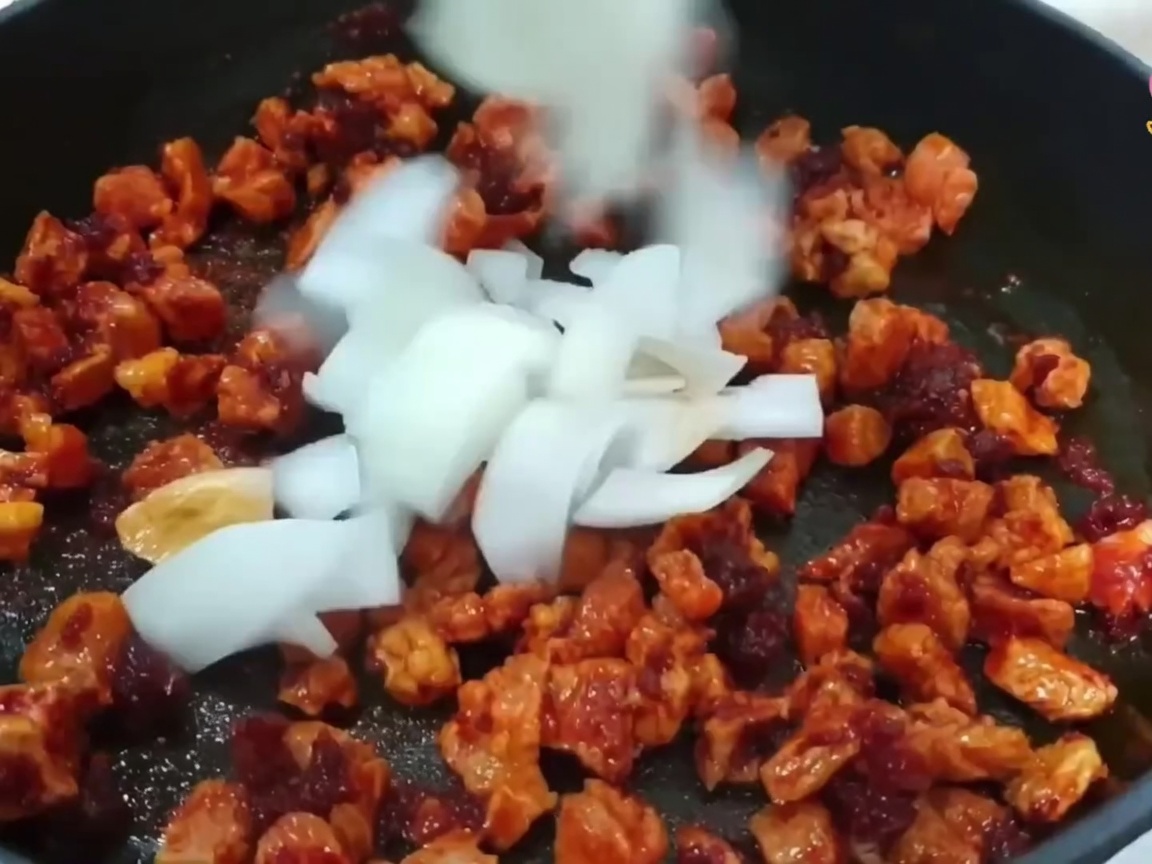 Cebolla picada, cebolleta y ajo añadidos a la sartén con el cerdo en cocción.