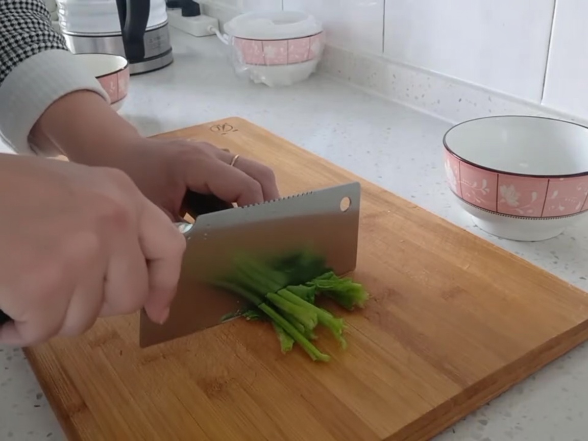 Hojas de espinaca verde fresca siendo cortadas en trozos pequeños sobre una tabla de cortar.
