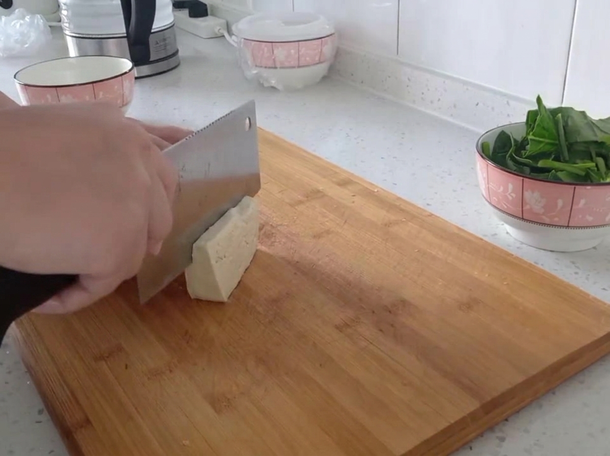 Un bloque de tofu firme siendo cortado en tiras finas y uniformes sobre una tabla de madera.