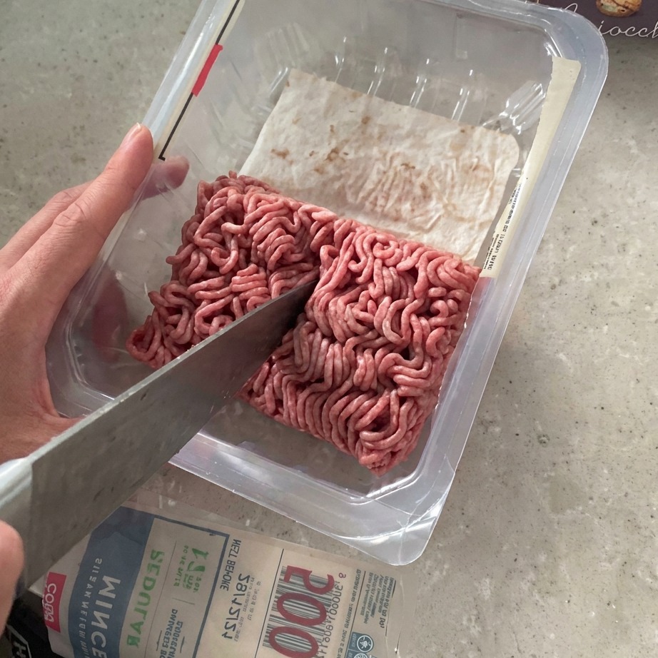 Carne picada siendo cortada por la mitad con un cuchillo grande dentro de su empaque.