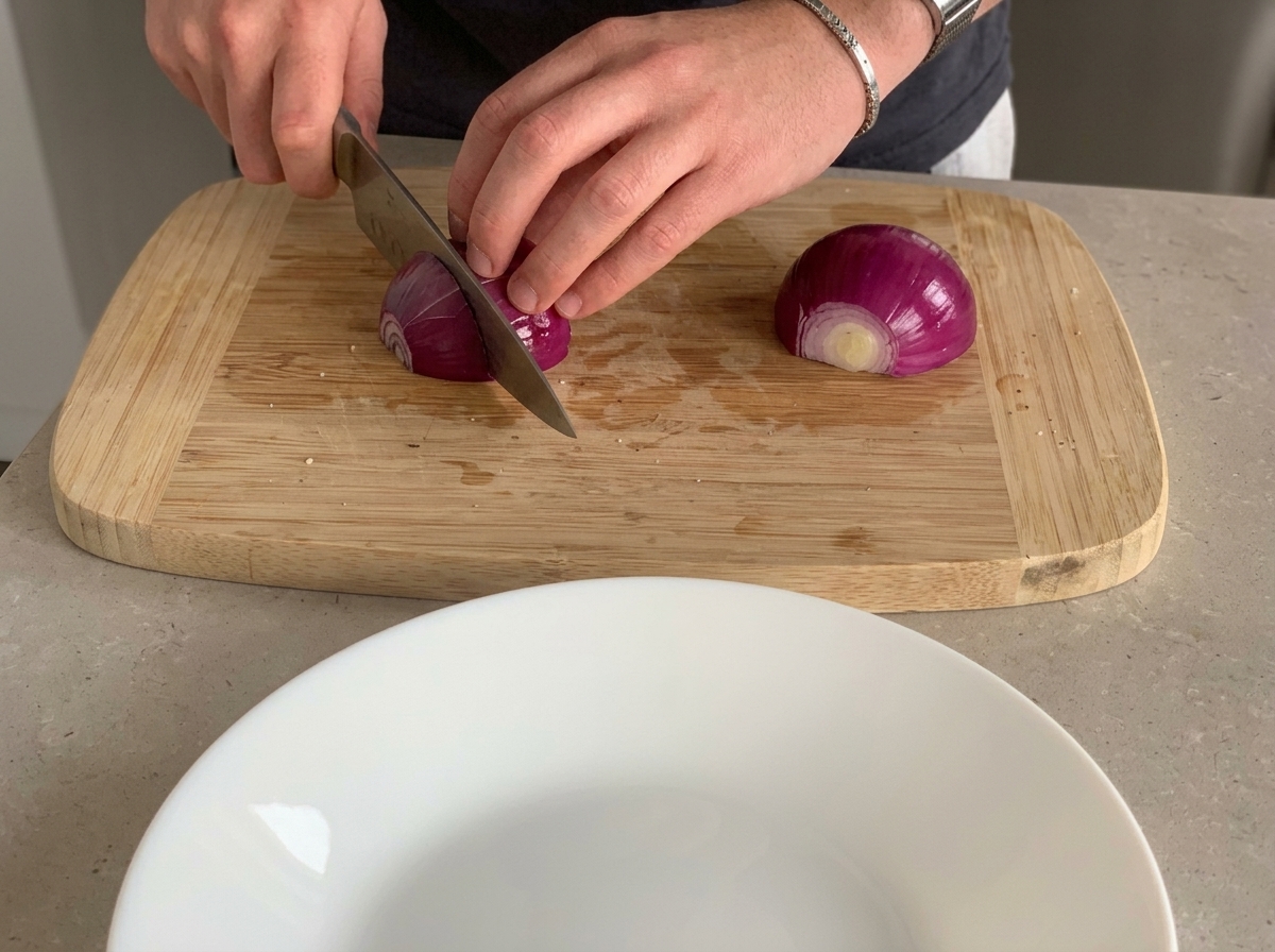 Cebolla morada siendo picada en trozos pequeños sobre una tabla de madera.